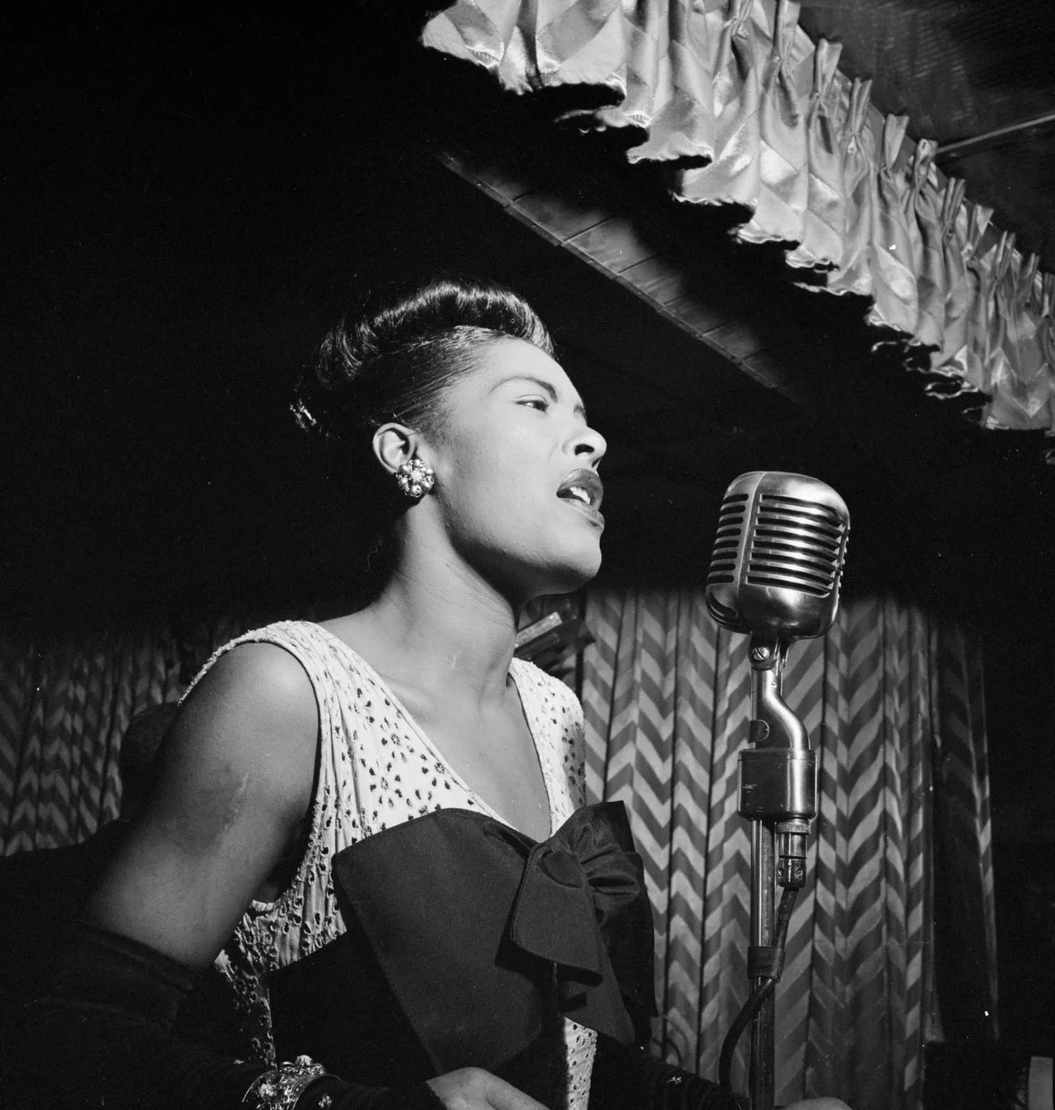 Vintage black and white photo of a Billie Holiday singing into a microphone.